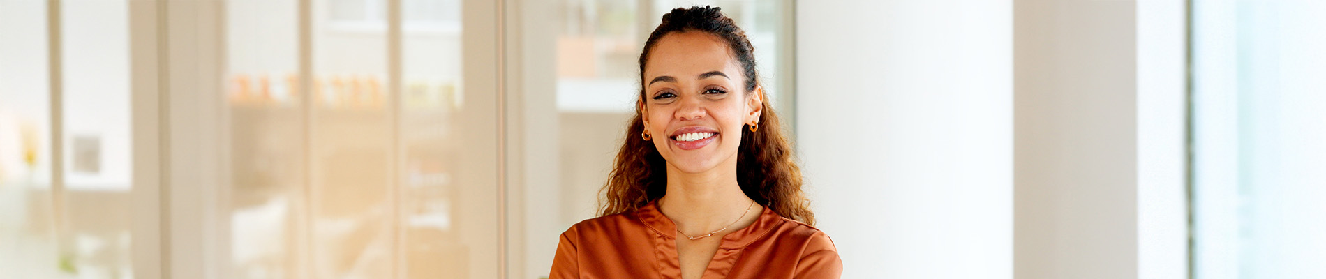 The image is a photograph of a woman with light skin, smiling at the camera. She appears to be in her late twenties or early thirties and has long hair. Her eyes are looking directly at the camera, and she is holding up her index finger near her mouth as if she s making a point or emphasizing something. The background is plain and light-colored, which suggests that this could be a stock photo used for various purposes such as advertising, personal branding, or lifestyle content.