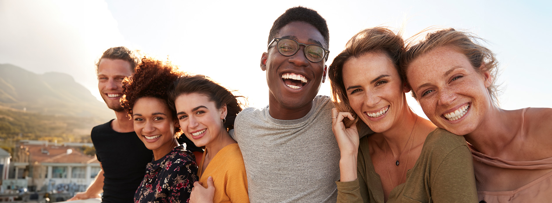 The image shows a group of people, possibly professionals given their attire and the setting that appears to be an office or professional environment. They are gathered around a table with a laptop on it, engaged in what seems to be a discussion or meeting.
